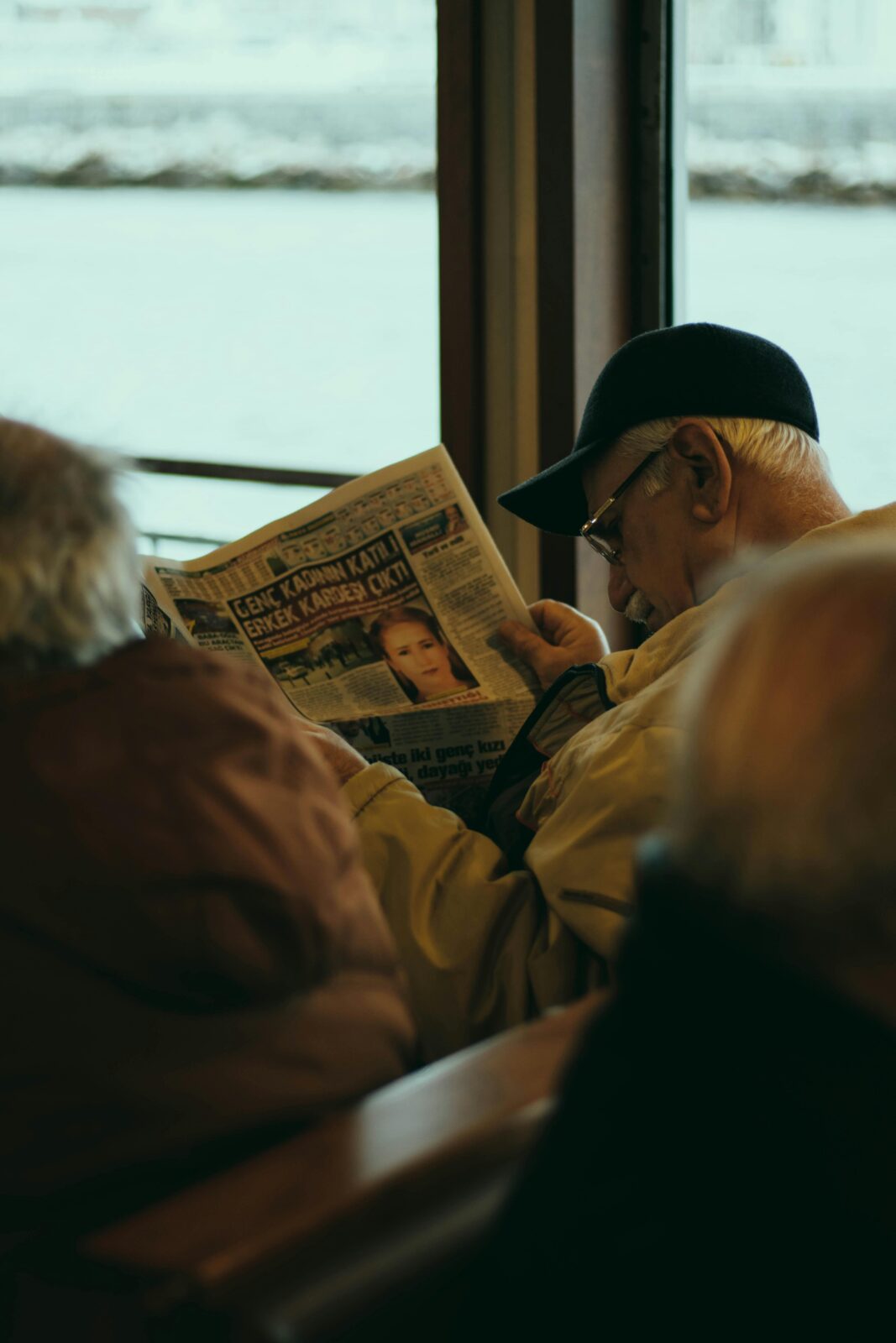 Elderly man in eyeglasses reads newspaper on a bus, illustrating travel lifestyle.