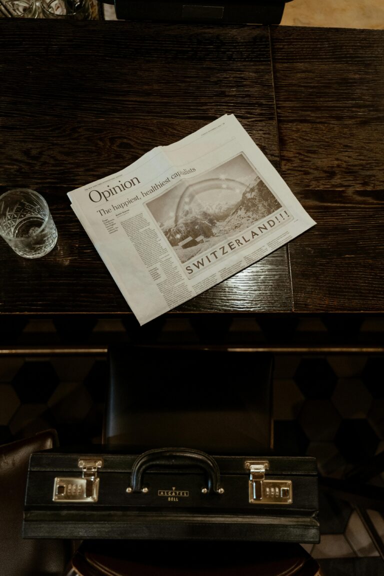 Top view of a newspaper and glass beside a briefcase on a vintage wooden table.