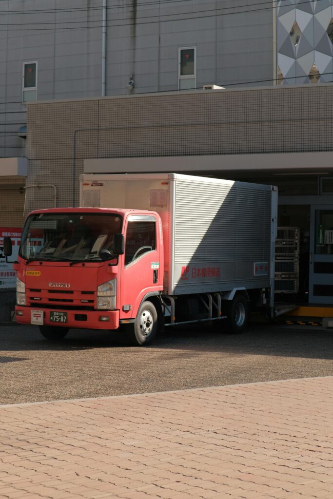 A red delivery truck unloading goods at a warehouse on a sunny day in the city.